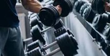 Person lifting a heavy dumbbell in a gym with a rack of weights.