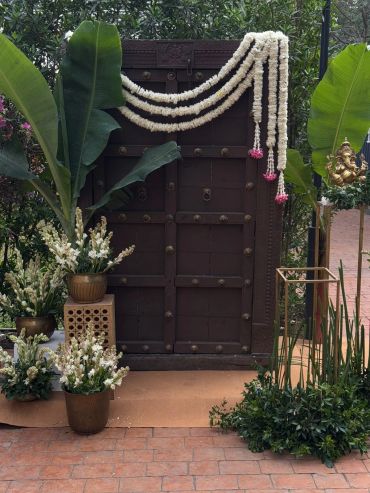 Traditional wooden door decorated with white flower garlands and potted plants.