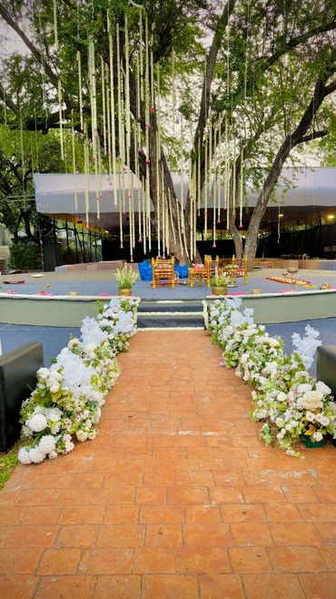 Elegant outdoor wedding stage with floral decorations and hanging garlands from a large tree.