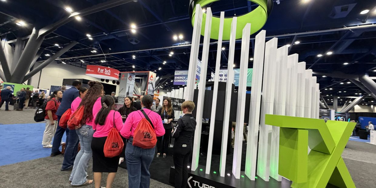 Group of people at a tech exhibition booth with large green TX letters.
