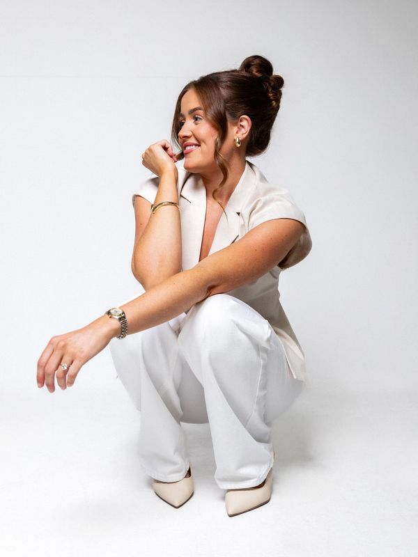 Woman in white outfit squatting and smiling to the side.