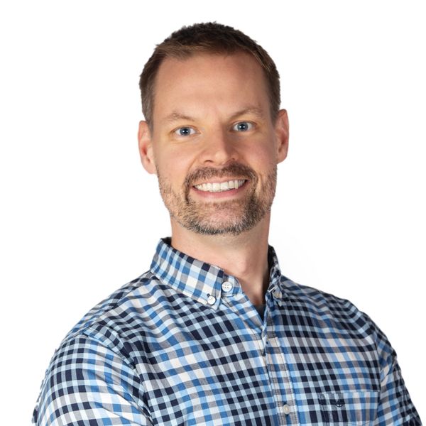 Smiling man in a blue checkered shirt against a white background.