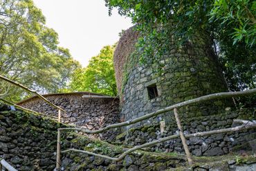Historic stone tower nestled in a lush green landscape, surrounded by wooden railings and trees