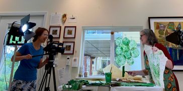 Two women joyfully filming an art project in a bright, cozy room.