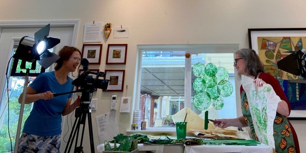 Two women joyfully filming an art project in a bright, cozy room.