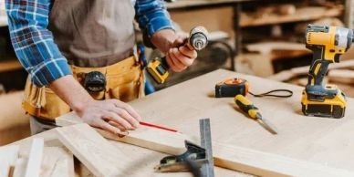 Person measuring and marking wood in a workshop with tools around.