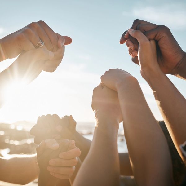 People holding hands together in unity with sunlight in the background.