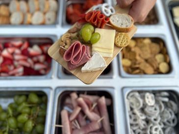 Hand holding a charcuterie board with meats, cheeses, grapes, and crackers.