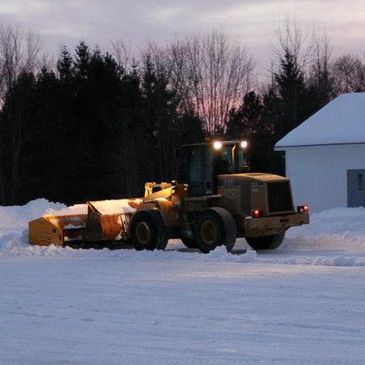 Snowplow clearing snow near a building at sunset.