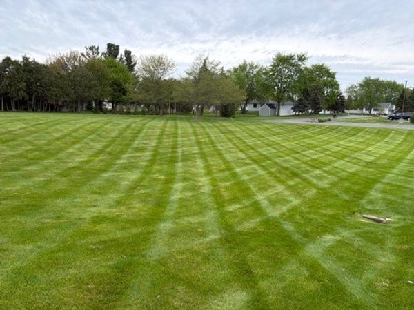 Freshly mowed green lawn with striped patterns under a cloudy sky.