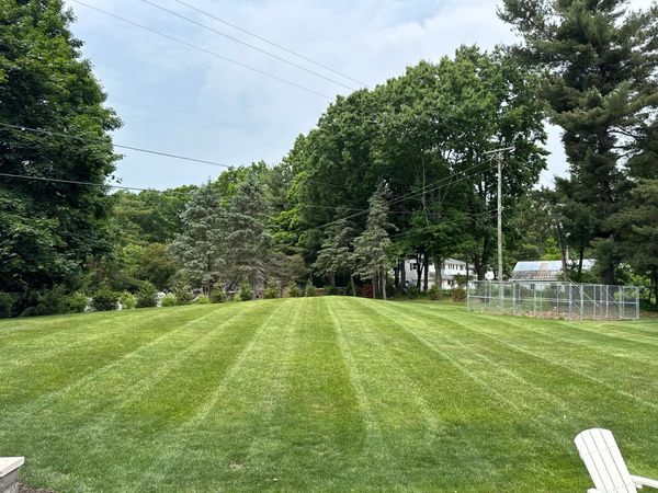A neatly mowed lawn with trees and a fenced garden area under a partly cloudy sky.