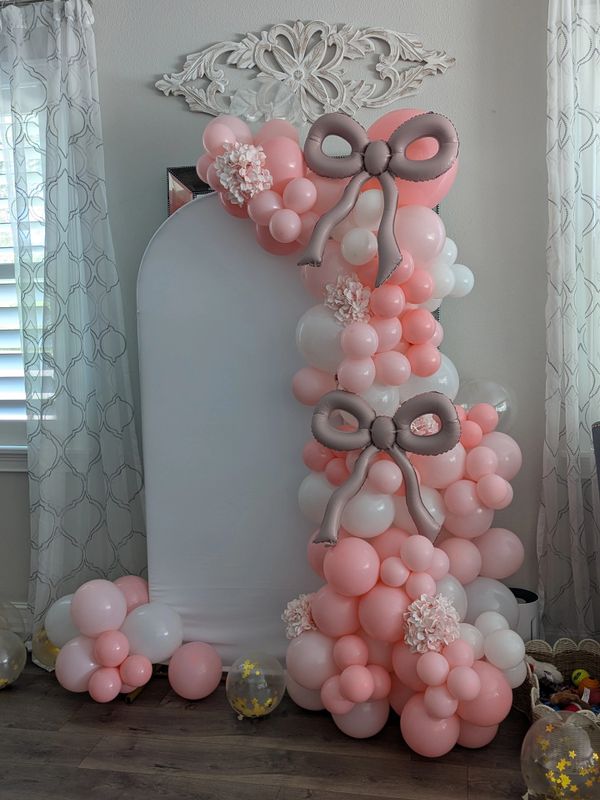 Pink and white balloon arrangement with bows and flowers.