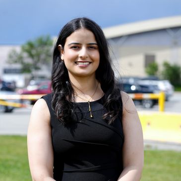 Young woman smiling outdoors in black dress.