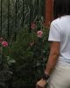 Person in white shirt near tall green plants with pink flowers.