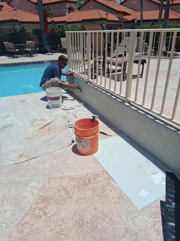 Man painting poolside wall near fence.