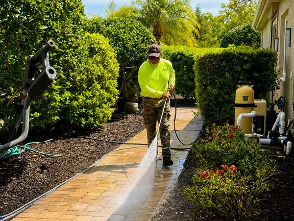 Person pressure washing a brick pathway on a sunny day.