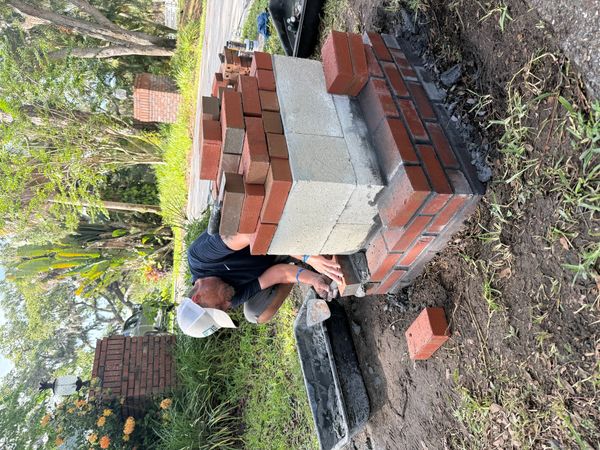 Worker installing brick pavers to concrete mailbox base