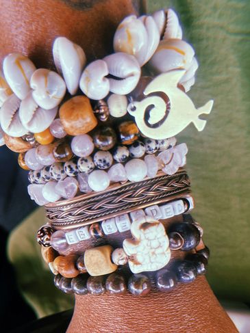 Stack of beaded bracelets with shells and charms on a wrist.