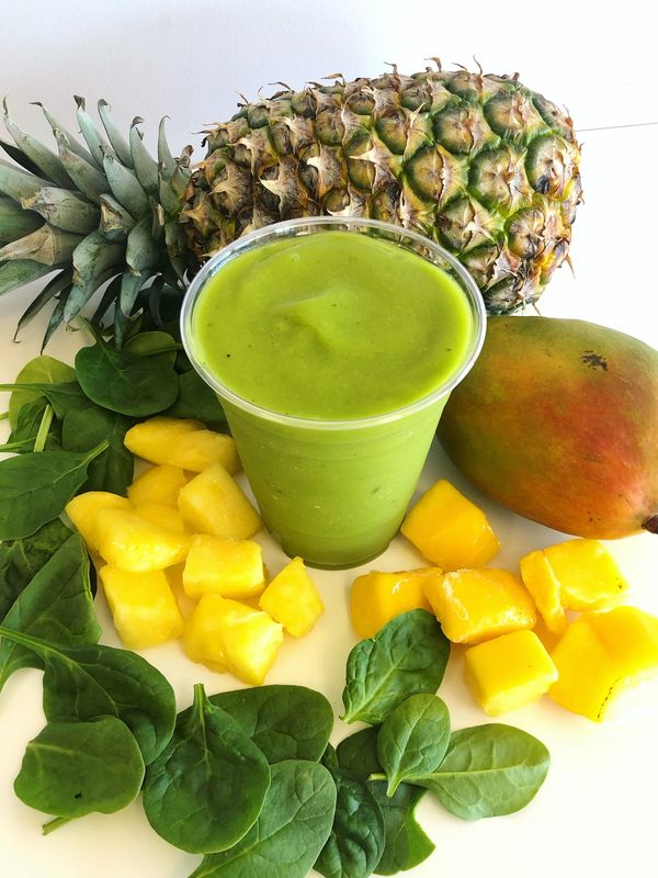 Green smoothie surrounded by pineapple, mango, spinach, and pineapple chunks.