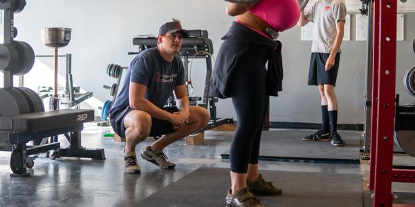 A man squats while coaching a woman lifting weights in a gym.