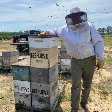 Beekeeper in protective gear tending to bee hives labeled BEE-LIEVE.