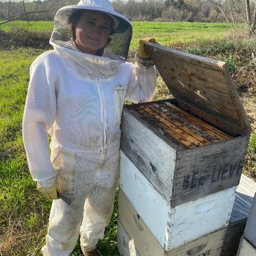 Person in beekeeping suit standing next to an open beehive.