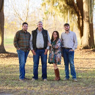 A family of four standing outdoors in a park during autumn.