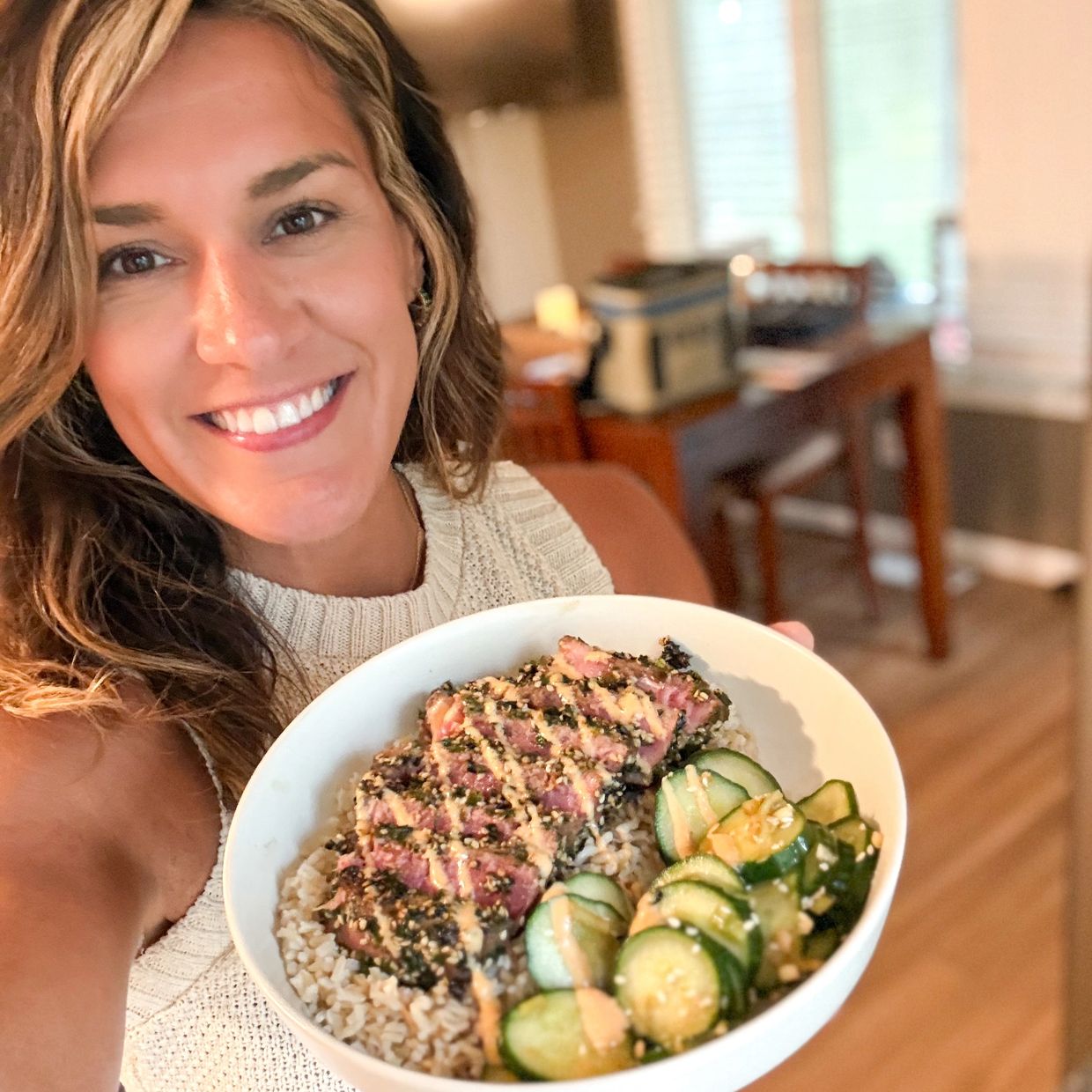 Smiling woman holding a bowl of rice, seared tuna, and cucumber.
