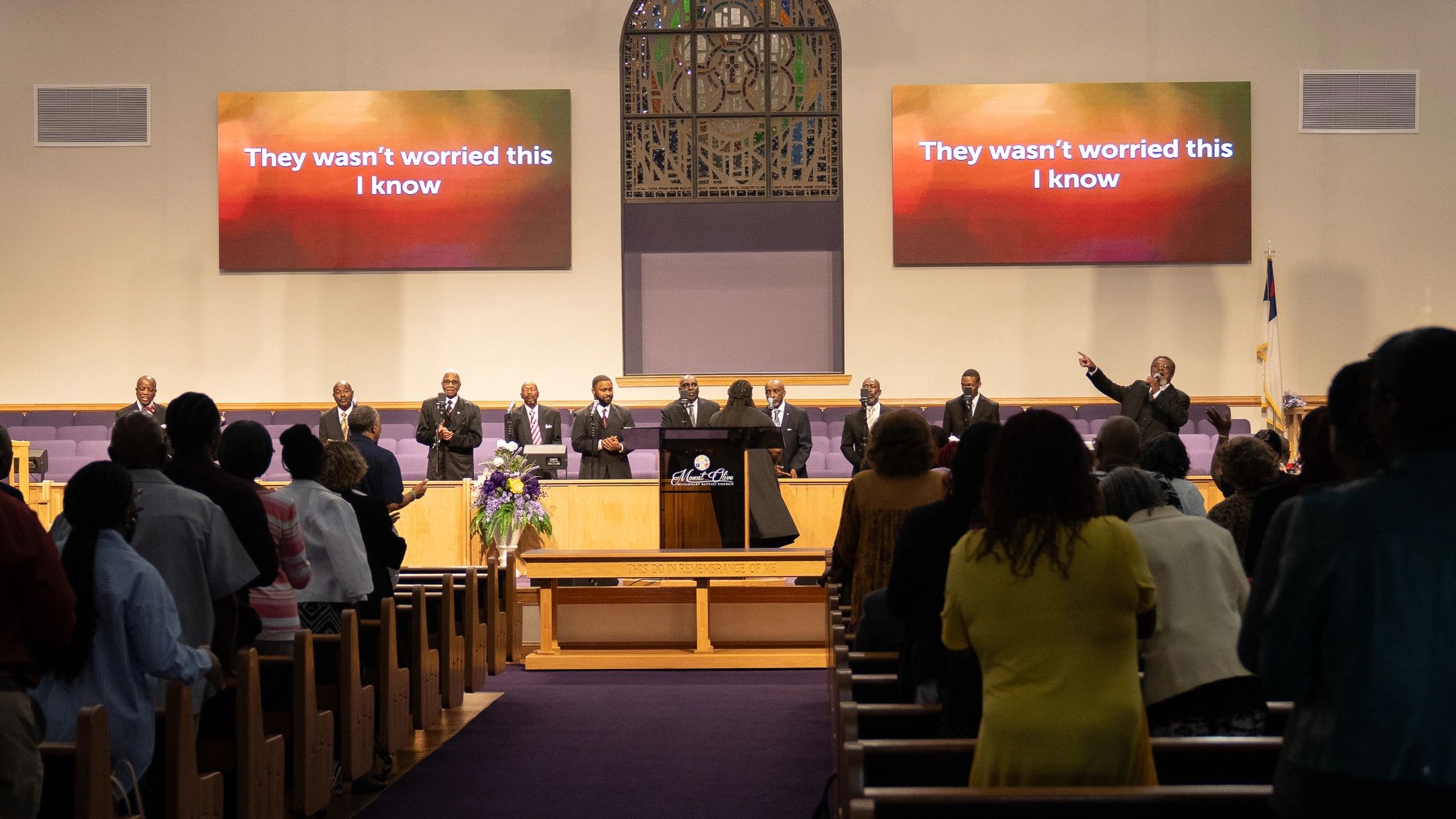 Congregation worships with choir and lyrics projected in church sanctuary.