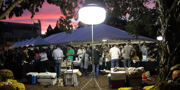 Outdoor evening event with tents and crowd under bright light.