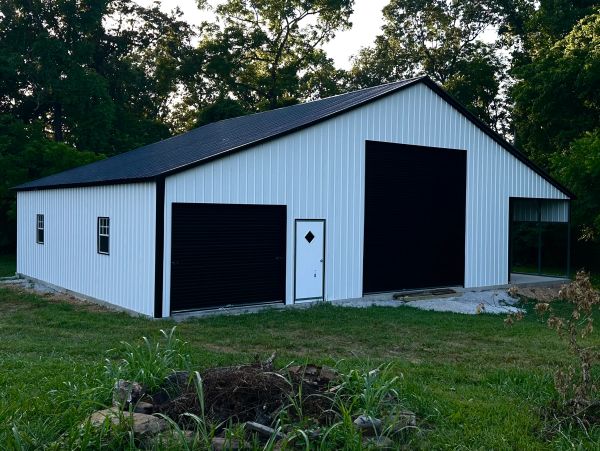 Large white metal building with black doors in a grassy area.
