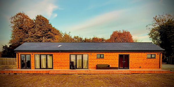 Modern wooden cabin with large windows and a dark roof under a blue sky.