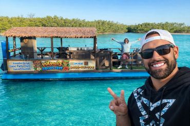 Two men smiling on a tiki tour boat in clear blue water.