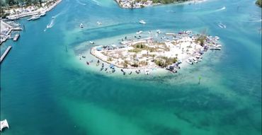 A small island surrounded by turquoise waters and boats in a sunny coastal area.