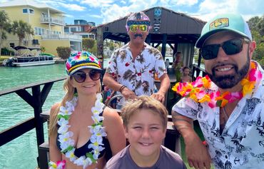 Family enjoying a boat ride with tropical leis and festive attire on a sunny day.