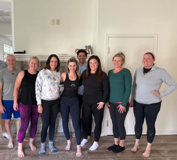 Group of eight adults standing barefoot indoors, smiling.