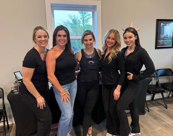 Five women posing together indoors, all smiling.
