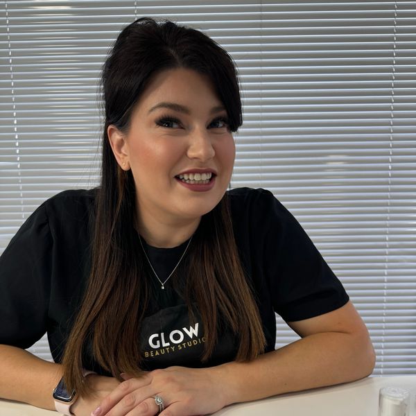 Smiling woman at Glow Beauty Studio with manicured nails and beauty products.