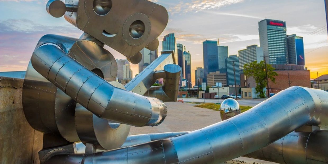 A large metal robot sculpture playing a guitar in front of a city skyline at sunset.
