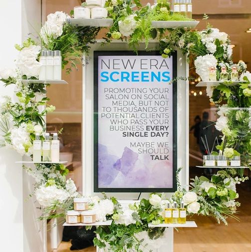 Salon window decorated with flowers & an advertising media screen