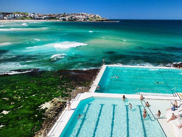 Beachside swimming pools overlooking the ocean with people swimming and relaxing.