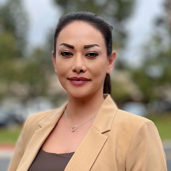 Professional woman in a beige blazer outdoors with a confident smile.