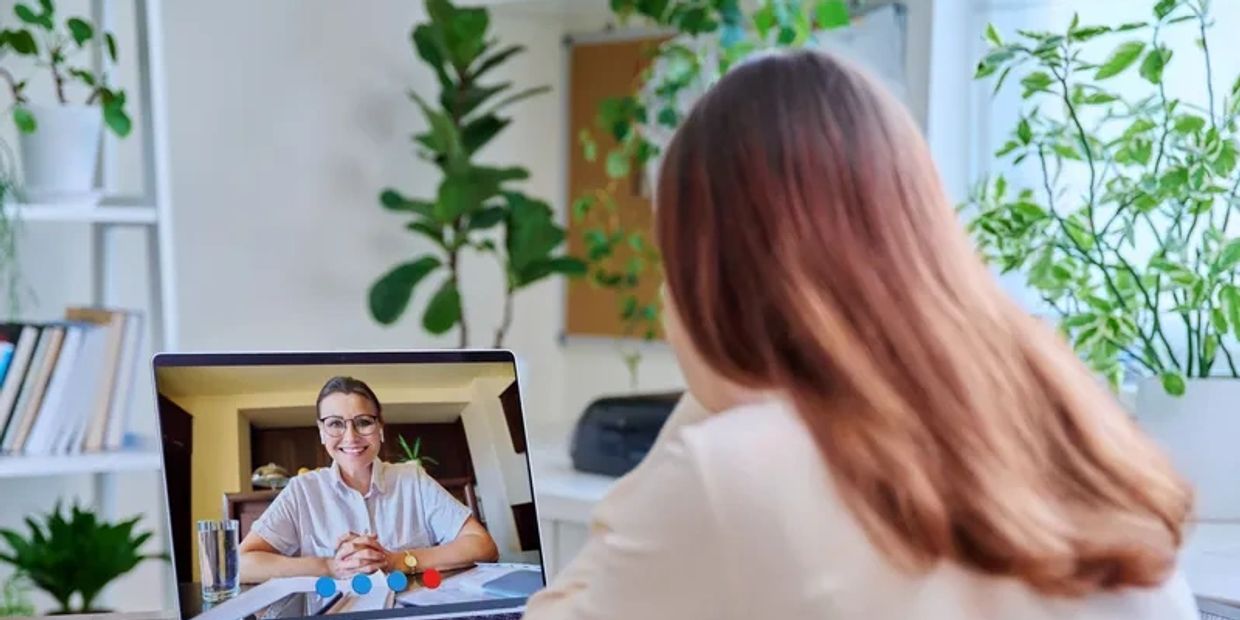 Two women engaging in a video call on a laptop in a cozy, plant-filled room.