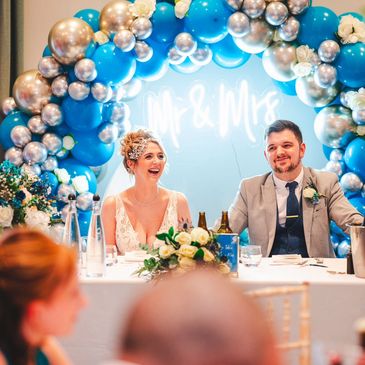 Bride and groom smiling at their wedding reception with blue and silver balloon decoration.