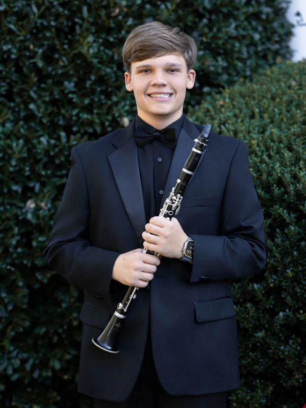 Young man in formal wear holding a clarinet outdoors.