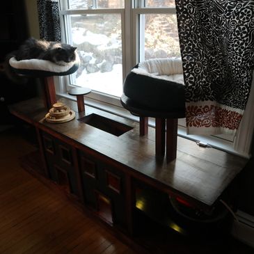 A fluffy cat rests on a cozy perch by a window with winter scenery outside.