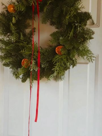 Green Christmas wreath with red ribbons and dried orange slices.