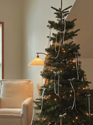 Minimalist Christmas tree with white ribbons and lights beside a cozy chair.