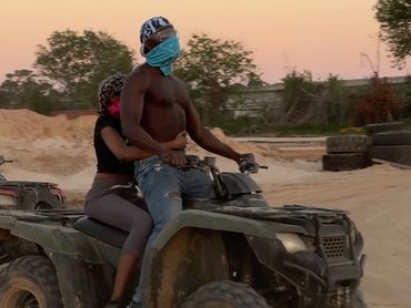 Two people riding an ATV on a dirt path at sunset.