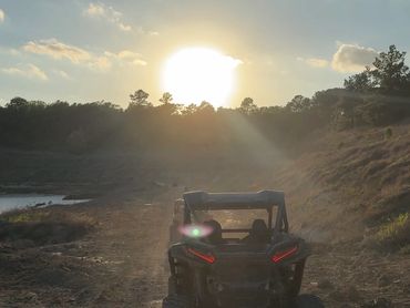 An off-road vehicle driving on a dirt path at sunset.